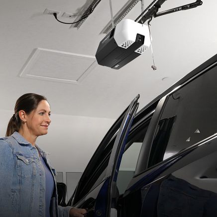Woman getting out of a car in a garage with a garage door opener above.