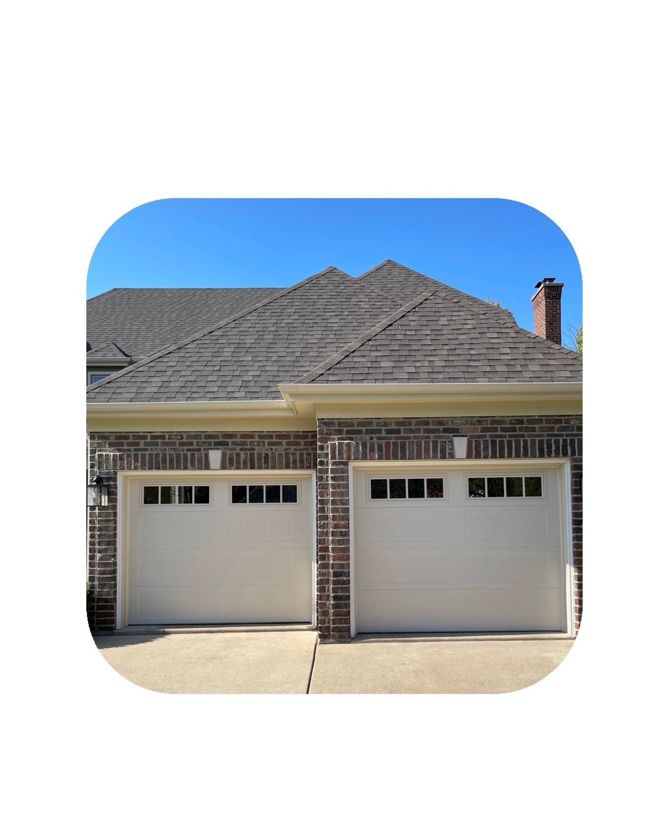 Two white garage doors with windows, red brick building, brown roof, blue sky.