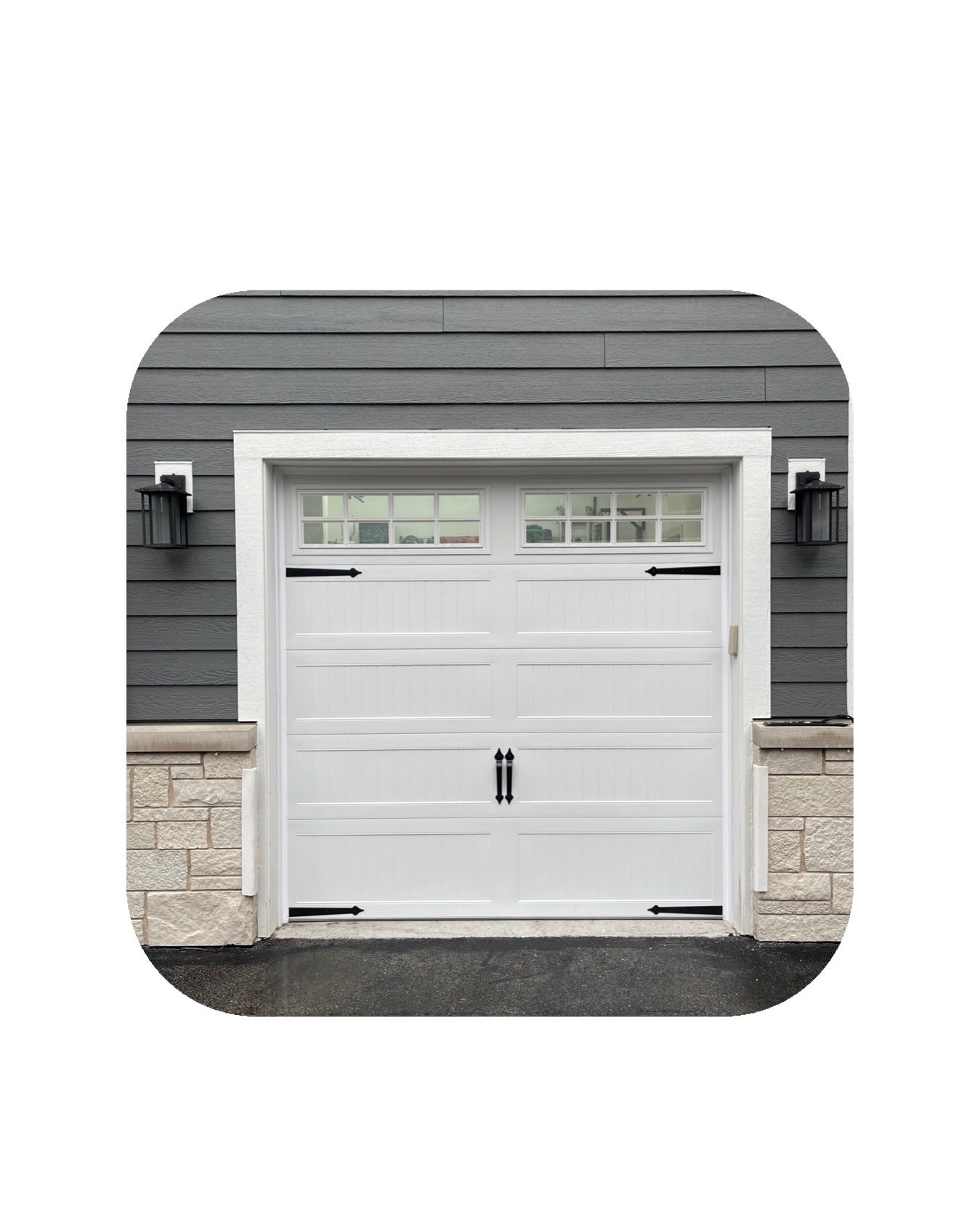 White garage door with windows, black hardware, gray siding, stone accents.