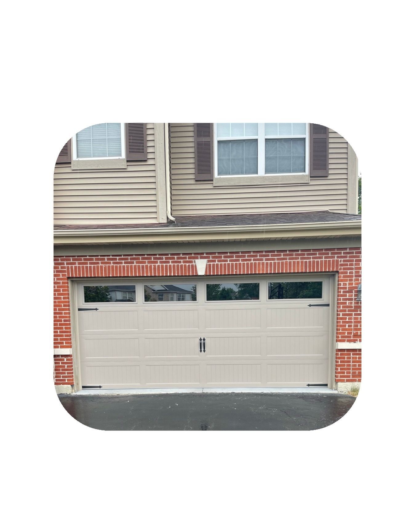 Tan garage door with windows, brick accents, and a beige house facade.