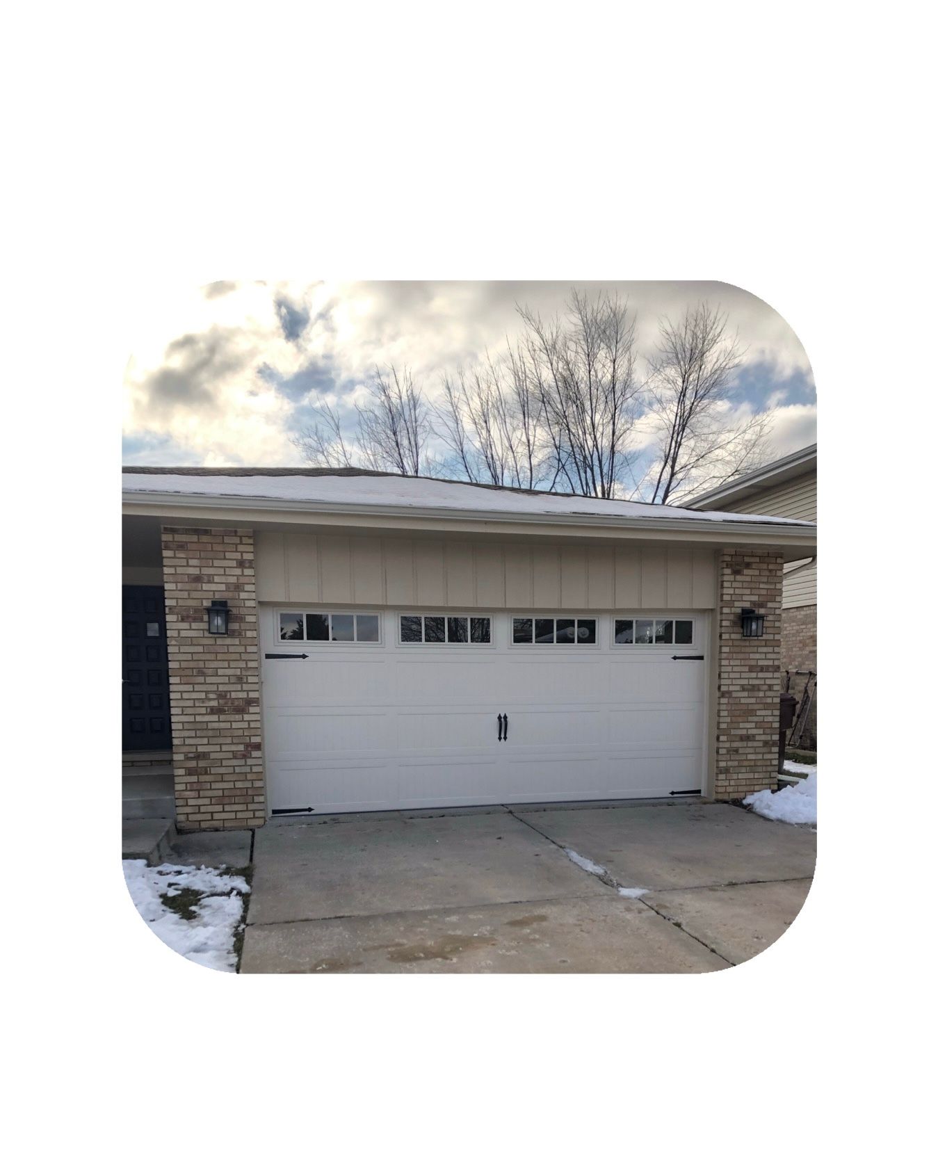 Garage with white door, brick accents, and snow on the roof. Cloudy sky in background.