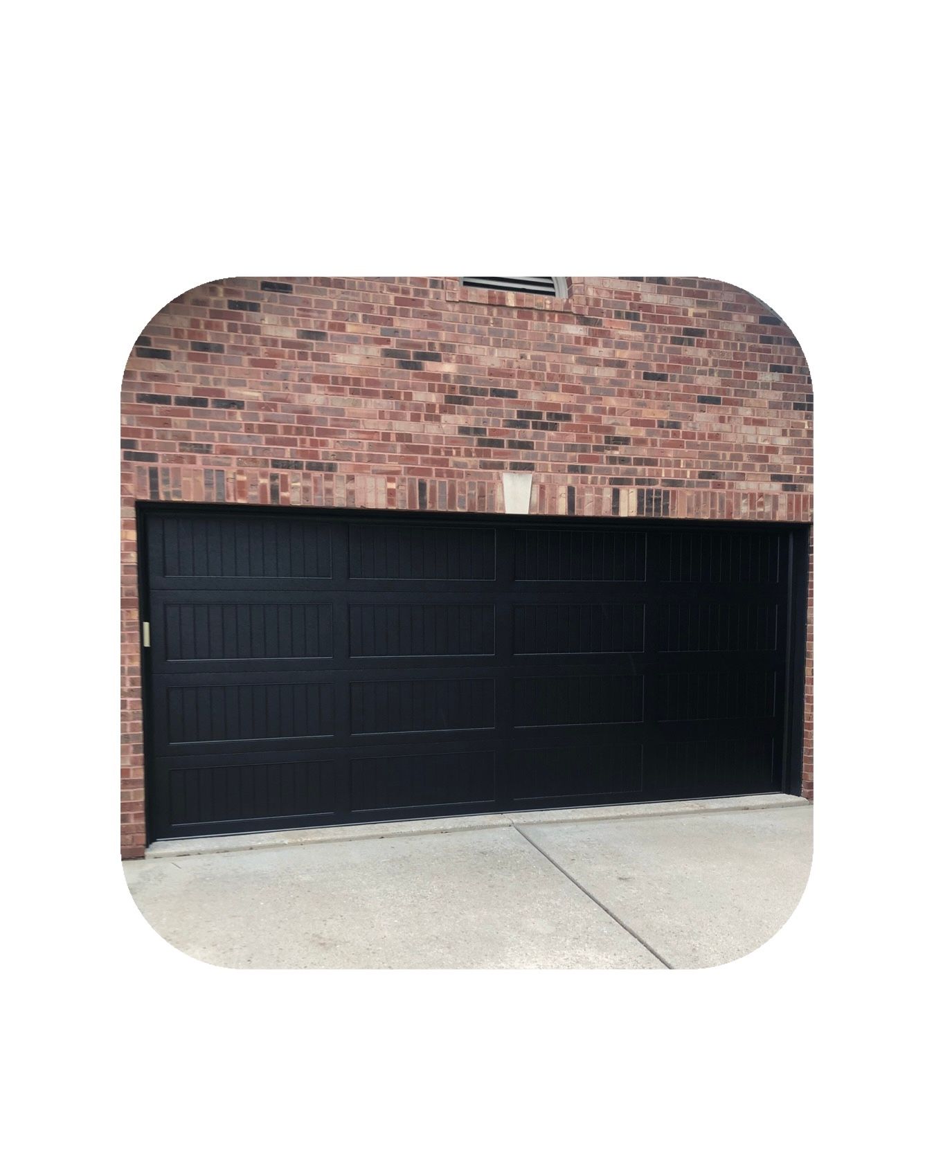Black garage door under a red brick building, set on a concrete driveway.