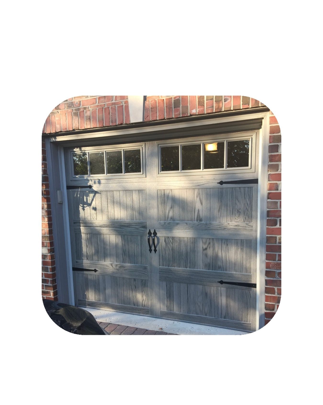 Gray garage door with windows, black hardware, set in a brick frame.