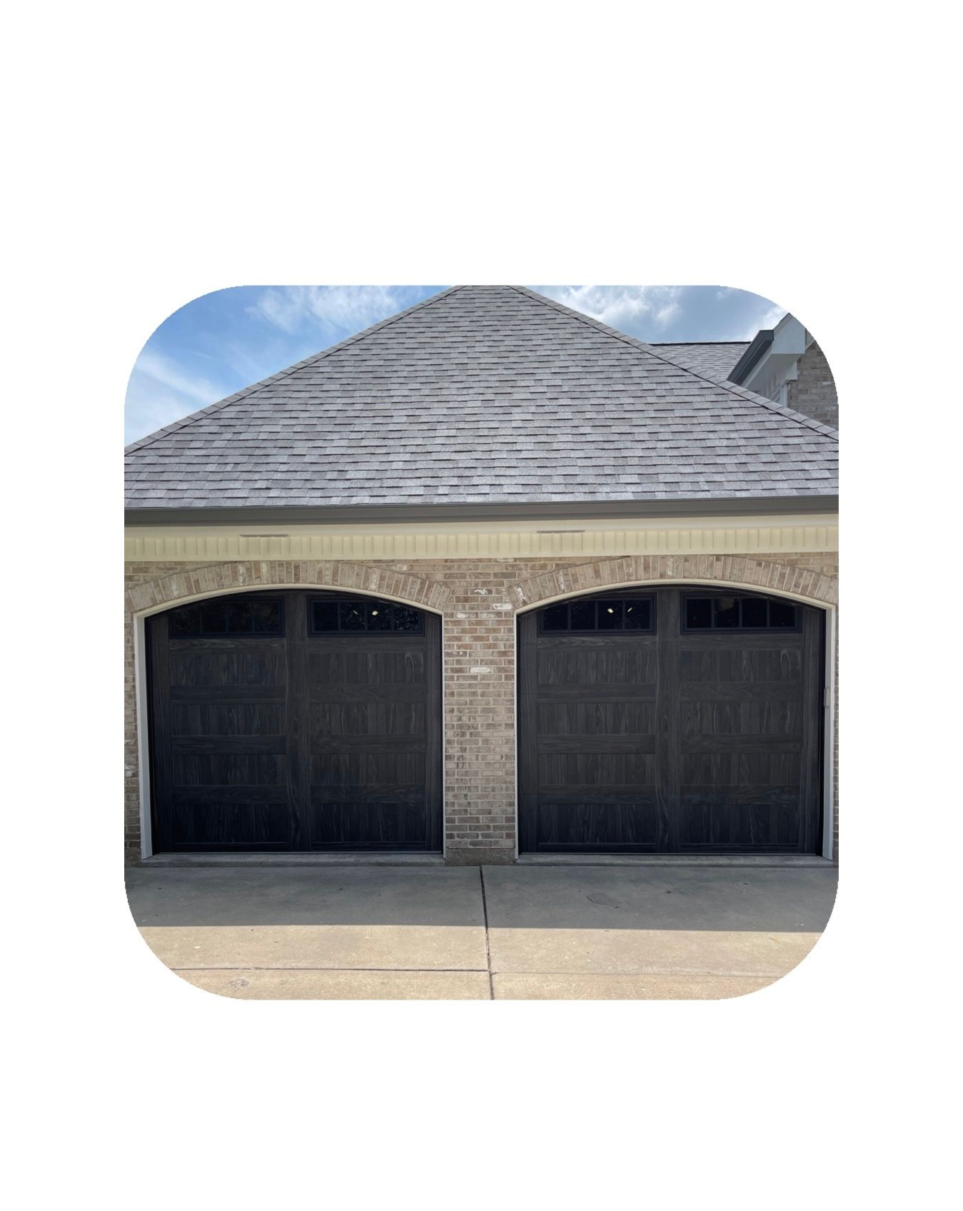 Double garage with dark doors, tan brick, and a grey shingle roof.
