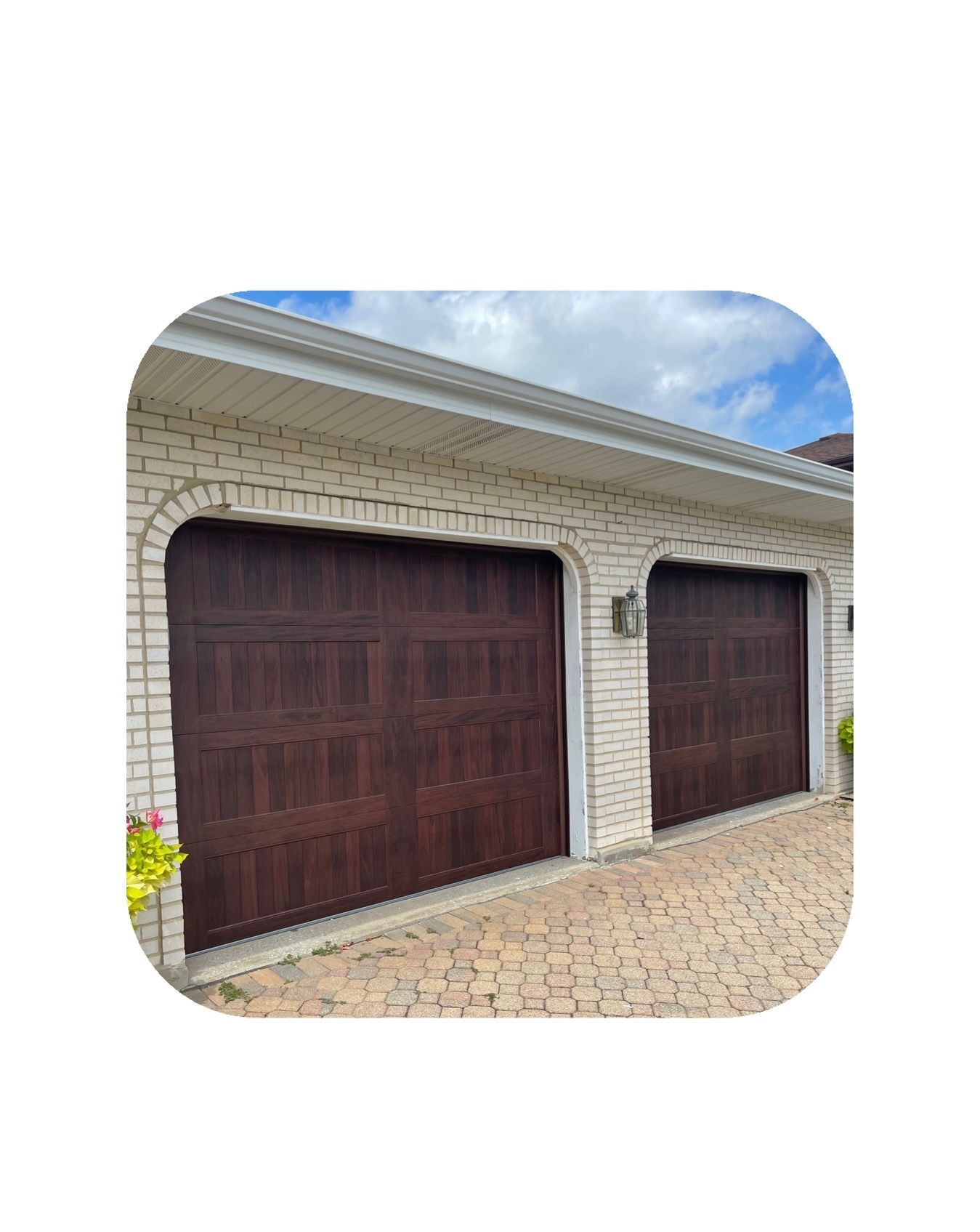 Two dark brown garage doors on a brick building with a patterned driveway.