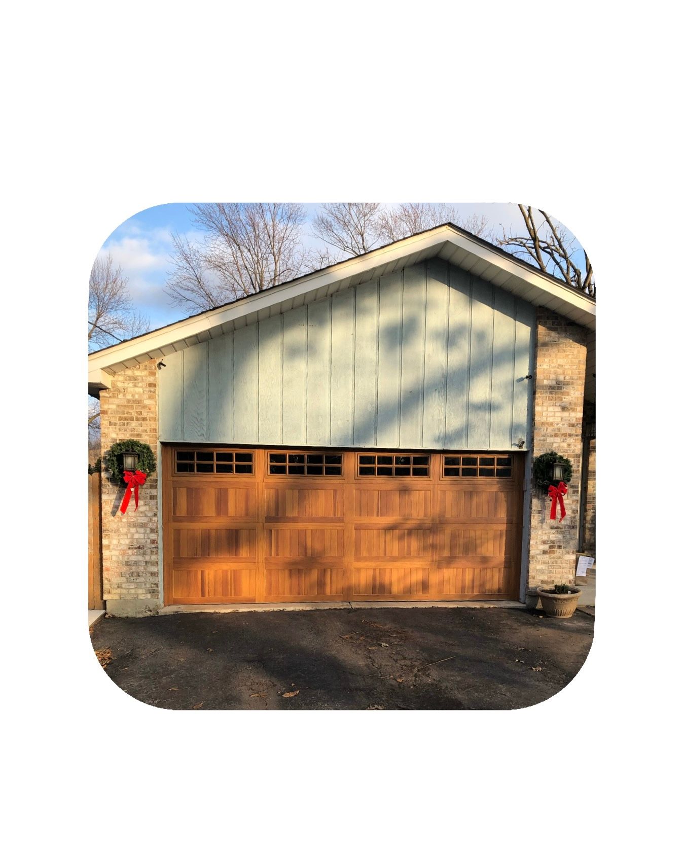 Brown garage door with brick and blue-green siding. Two wreaths with red bows hang on the garage.