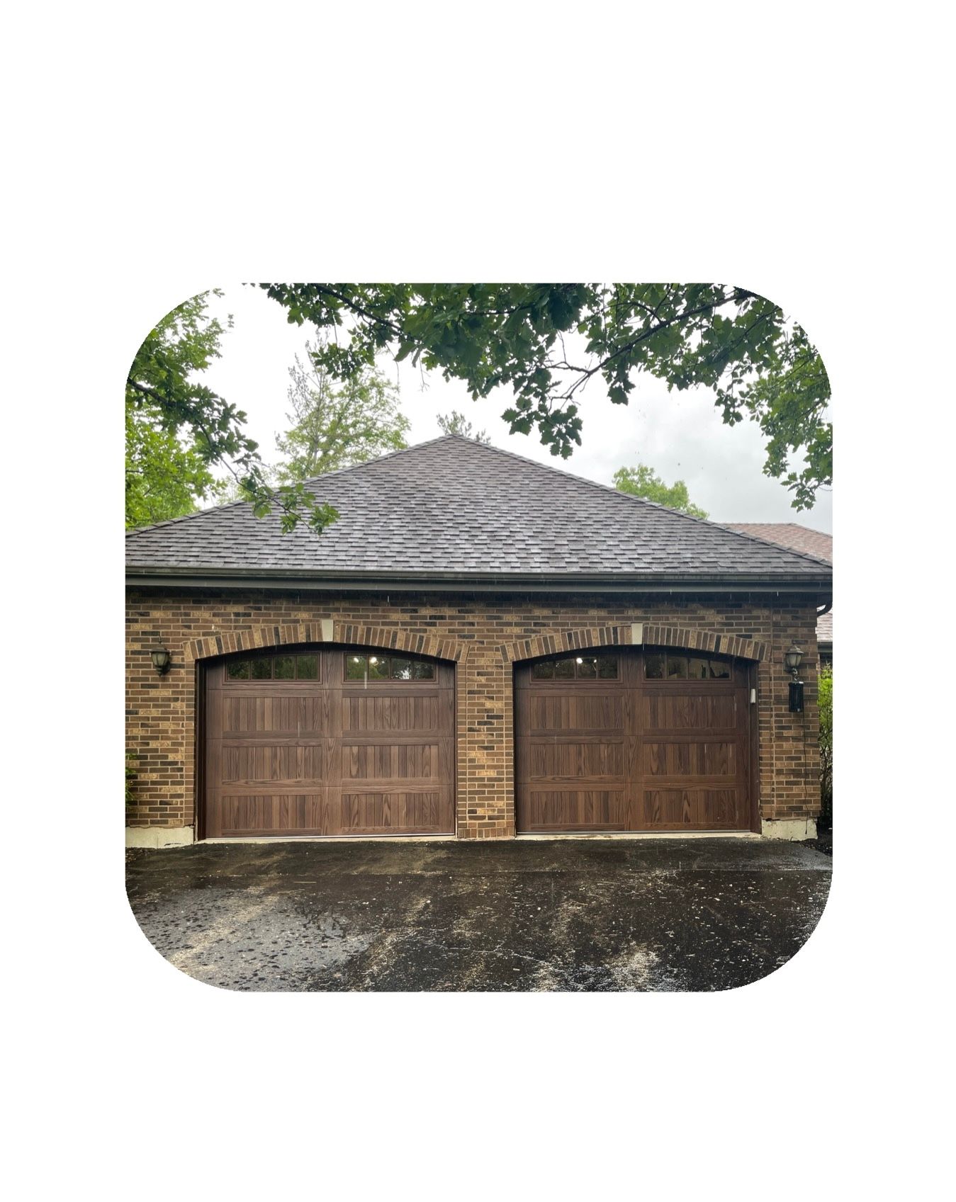 Stone garage with two brown doors under a slate roof, set against trees.