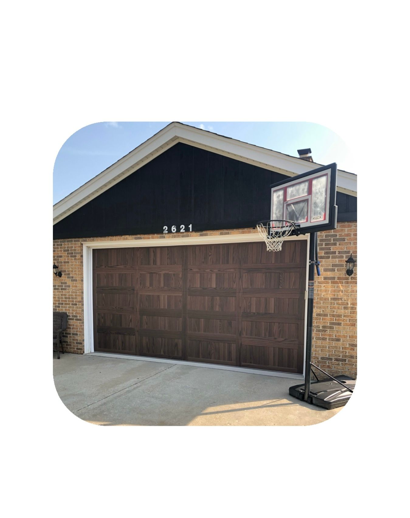Brown garage door, brick facade, basketball hoop, and a clear sky.