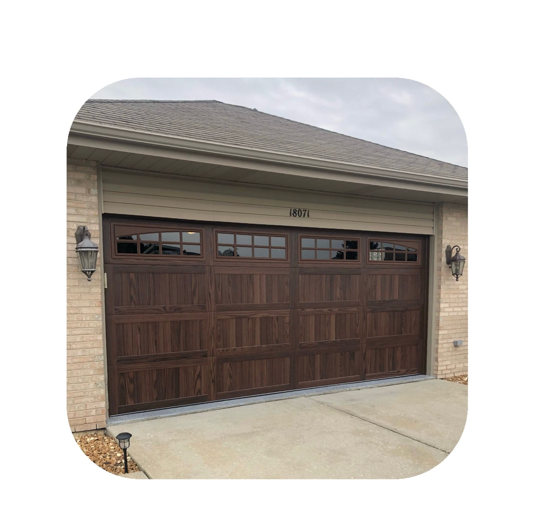 Dark brown paneled garage door with windows, on a beige brick house.