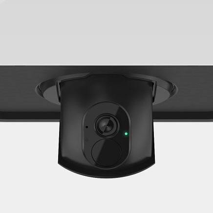 Black security camera mounted on a black surface, with a green status light.