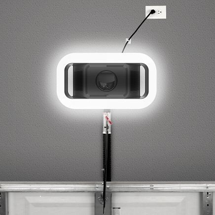 Garage door opener unit with built-in light, mounted to ceiling, cord plugged into an outlet.