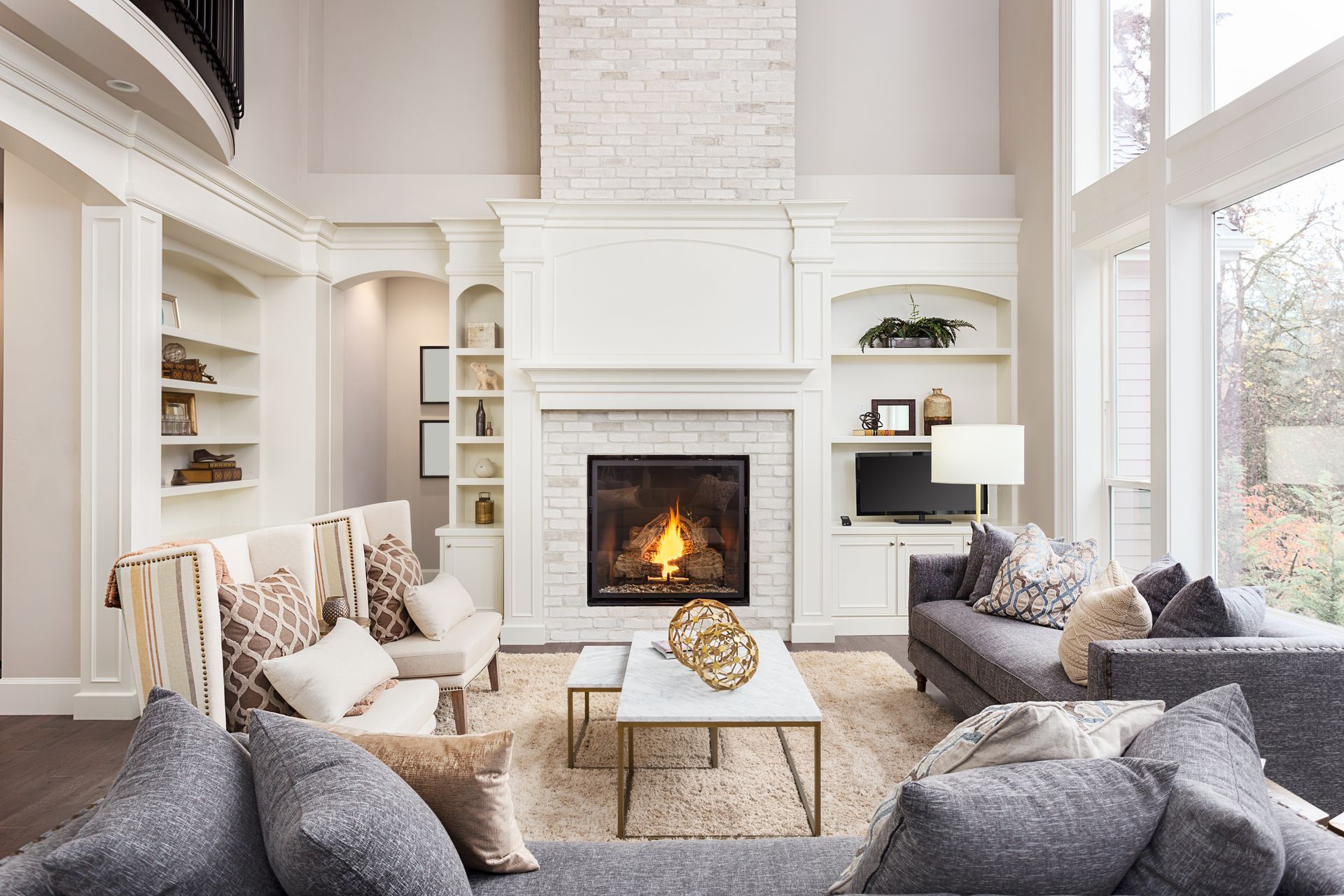 Bright living room with white fireplace, gray sofas, and large windows.