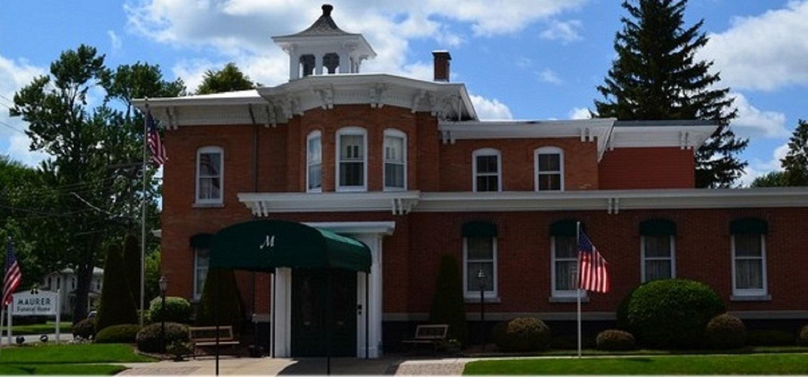 A two-story red brick building with a cupola and a green awning over the front entrance, featuring two American flags.