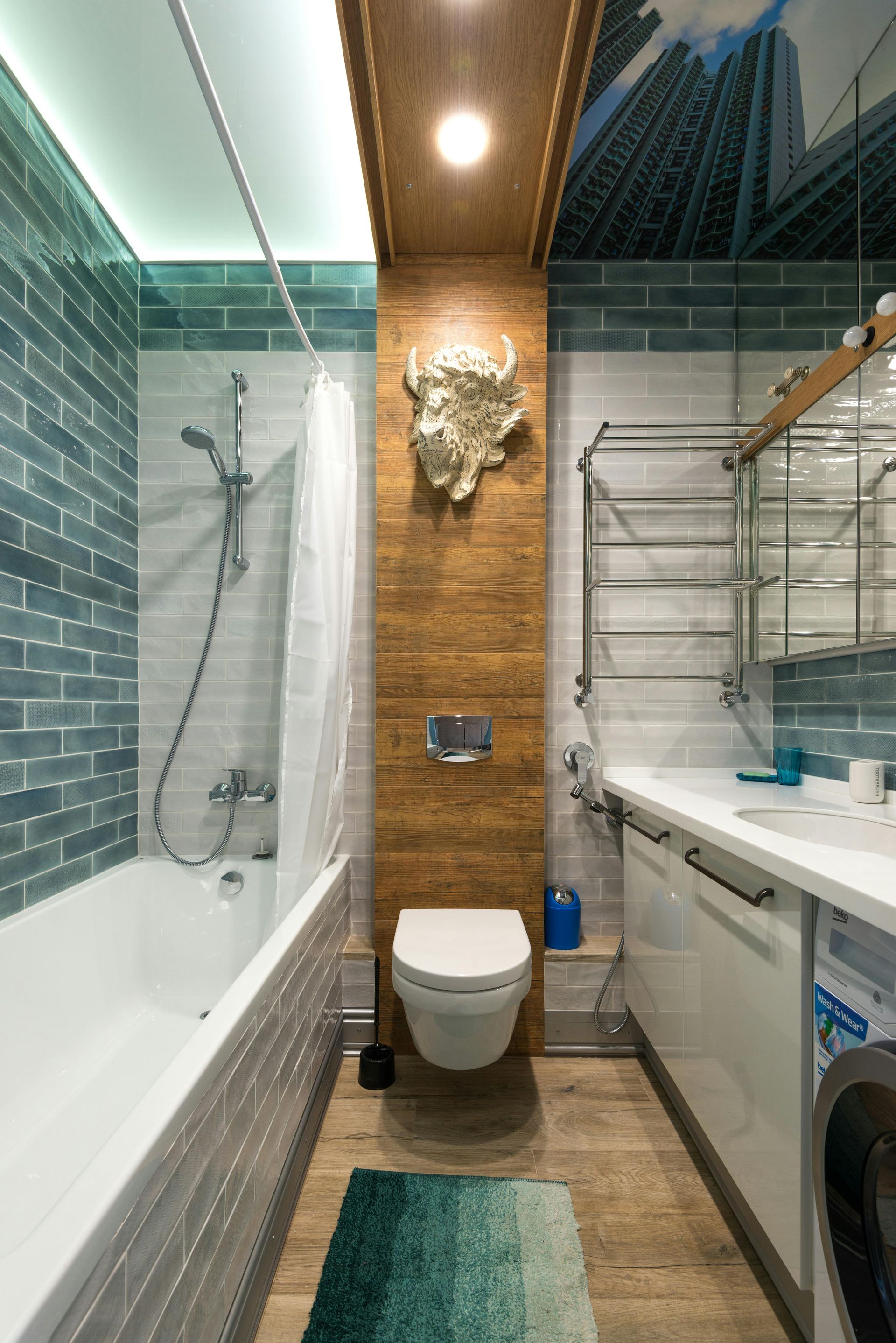 A modern bathroom featuring a white tub, wall-mounted toilet with a bison decor piece, and teal subway tile accents.
