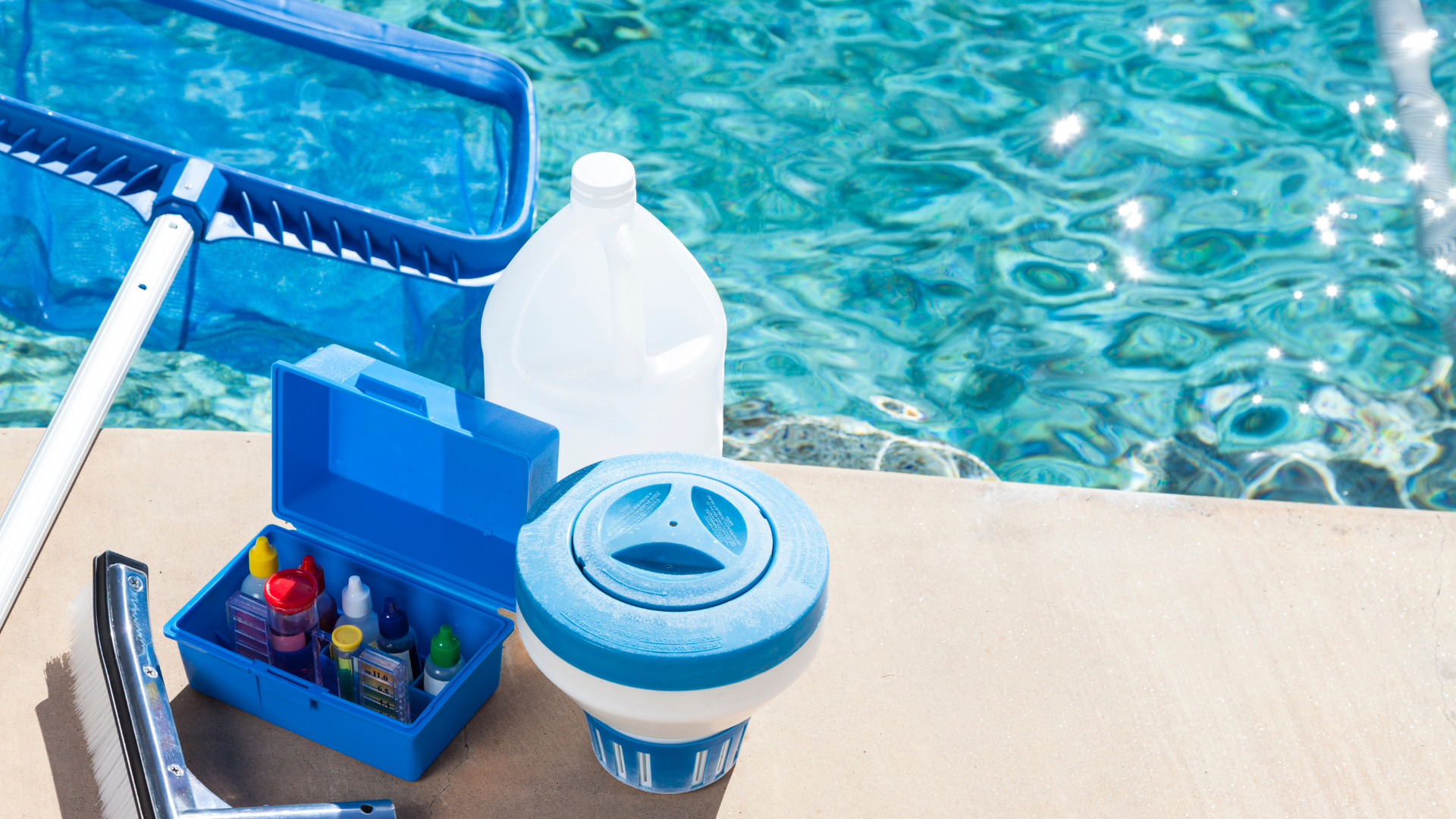 Pool cleaning supplies beside a blue swimming pool, with a skimmer net and chemical bottles on the deck