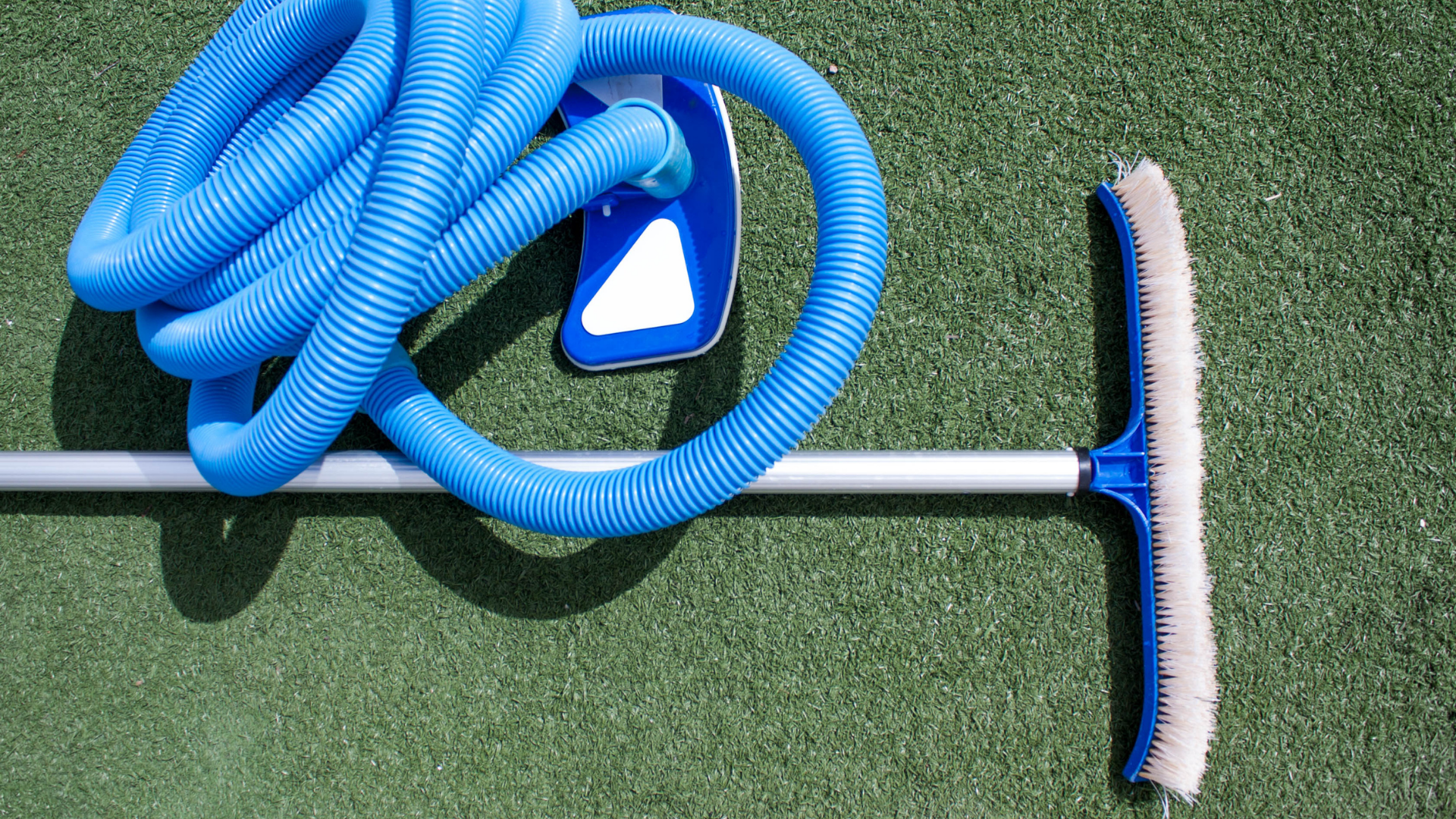 Blue coiled garden hose with spray nozzle and broom on green turf floor