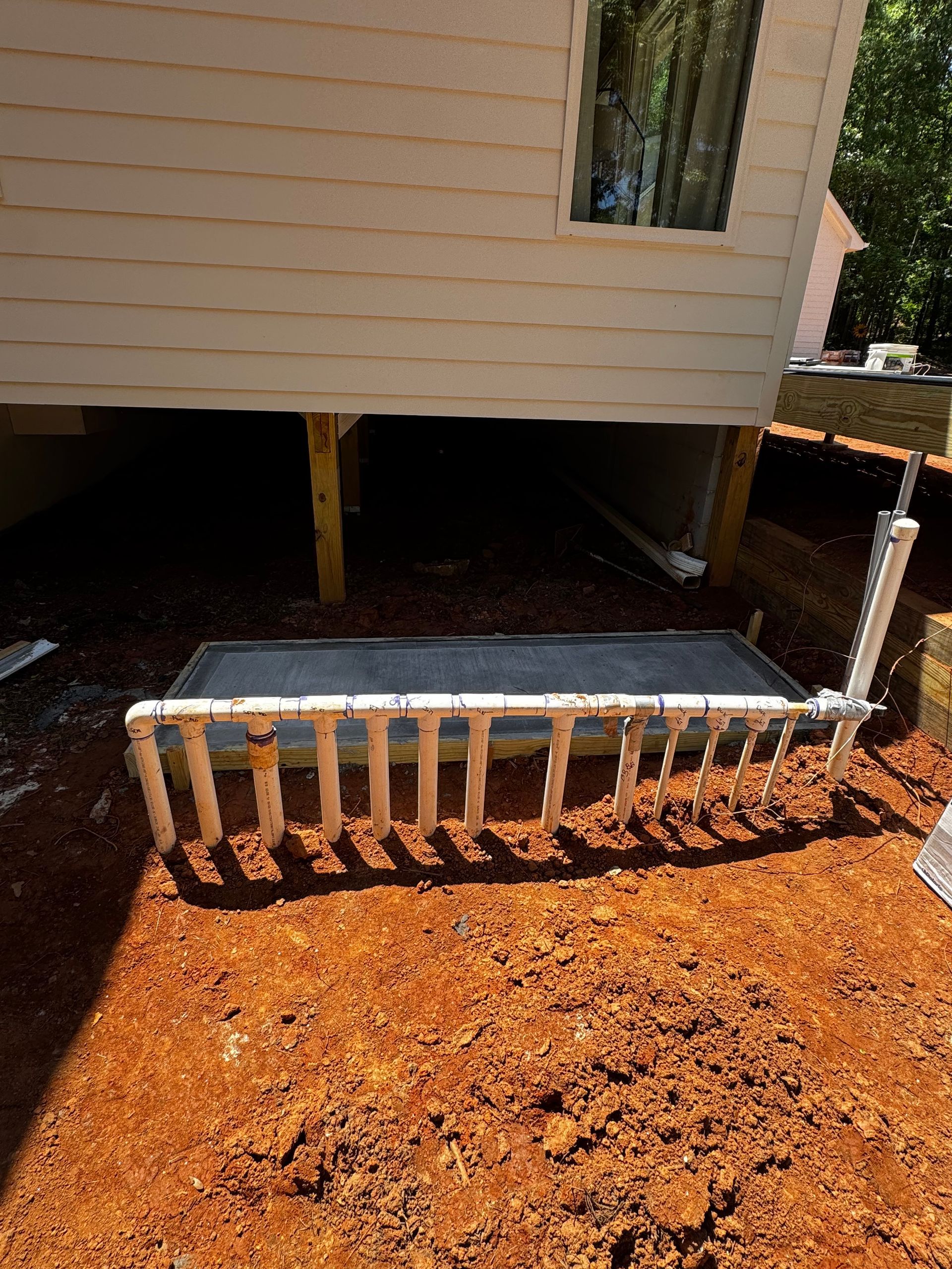 House foundation with a small vented platform and exposed pipes over reddish dirt ground
