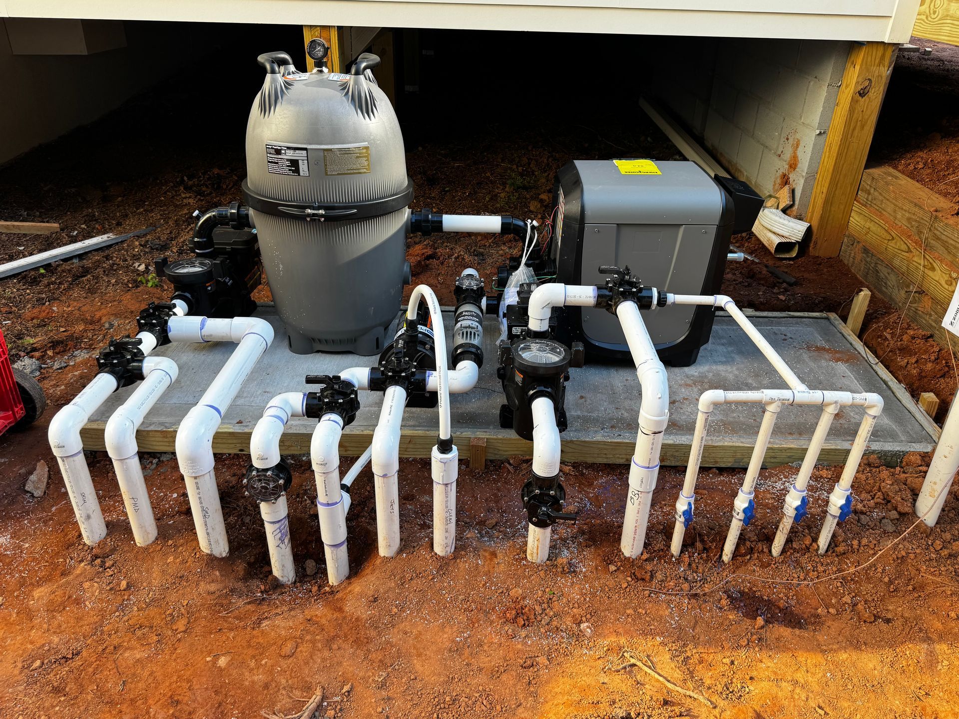 Outdoor water filtration system with gray tank, black pipes, and white PVC piping under a structure