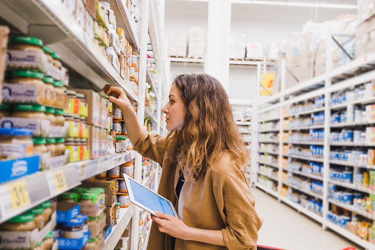 Uma mulher está olhando para um pote de manteiga de amendoim em um supermercado.