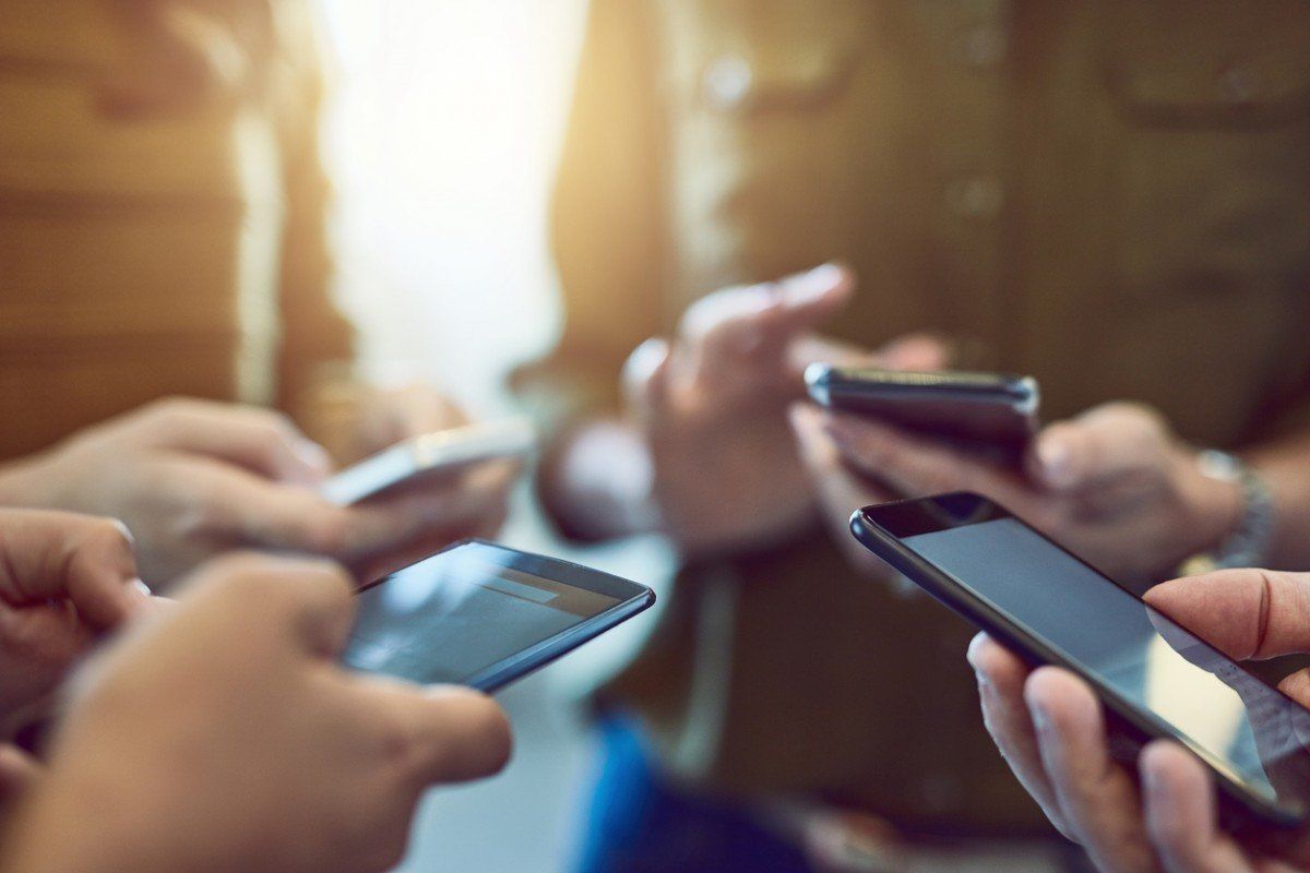 Um grupo de pessoas segura celulares nas mãos.
