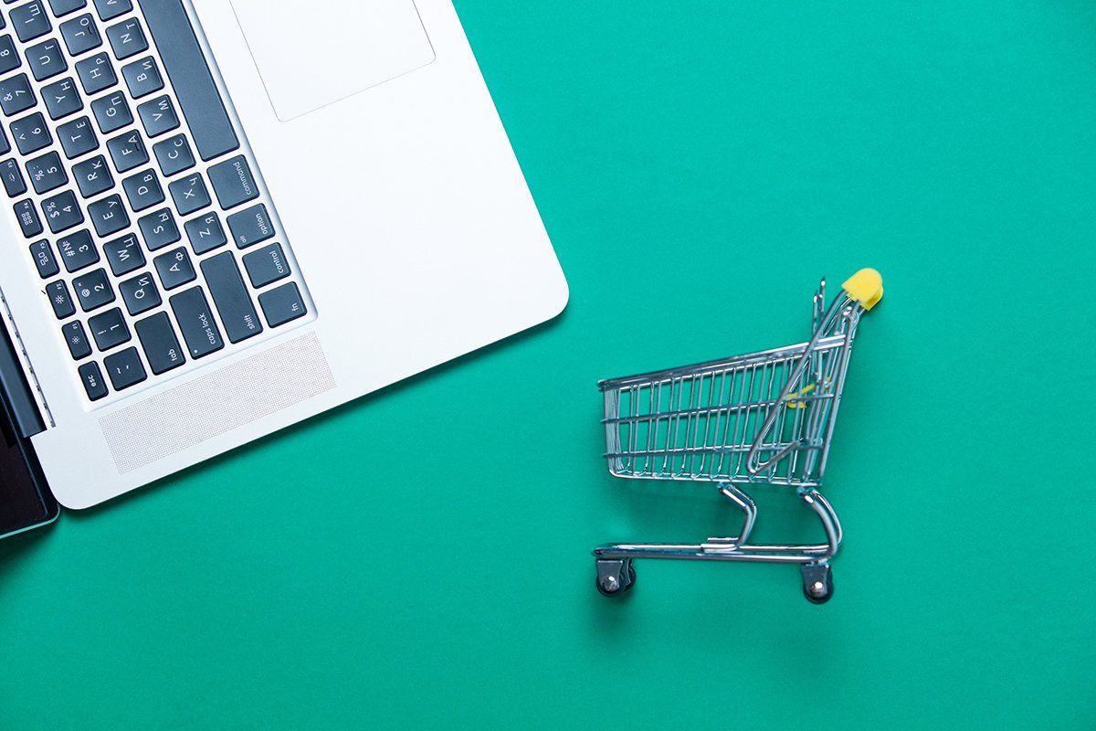 um carrinho de compras está ao lado de um laptop em uma mesa verde.