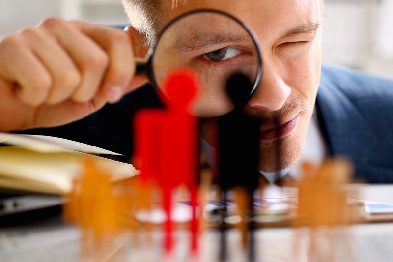 um homem está olhando através de uma lupa para uma figura vermelha.