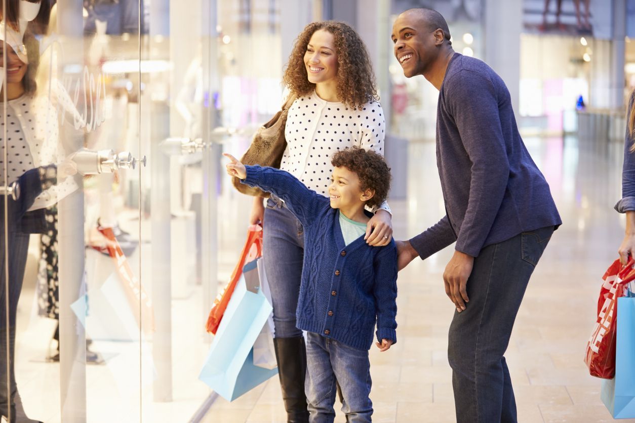 Uma família está fazendo compras em um shopping e olhando a vitrine de uma loja.