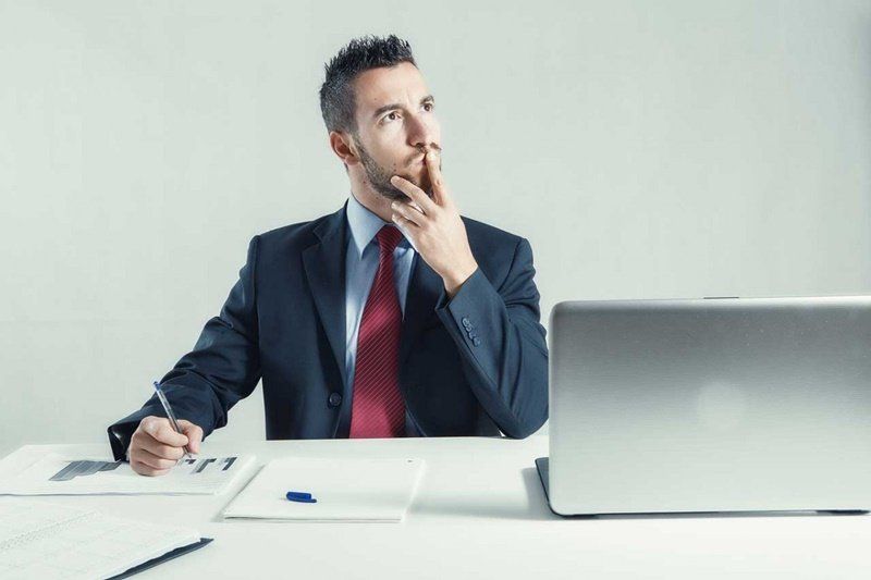 um homem de terno e gravata está sentado em uma mesa em frente a um laptop.