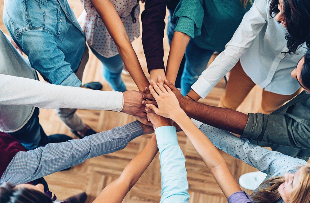 Um grupo de pessoas junta as mãos em círculo.