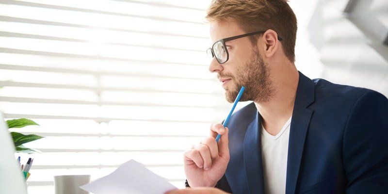 a man in a suit and glasses is sitting at a desk holding a piece of paper and a pen .