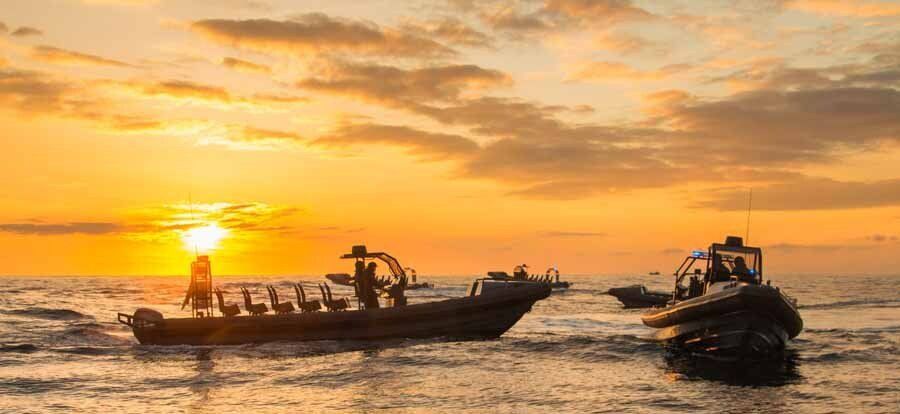 A group of boats are floating on top of a body of water at sunset.