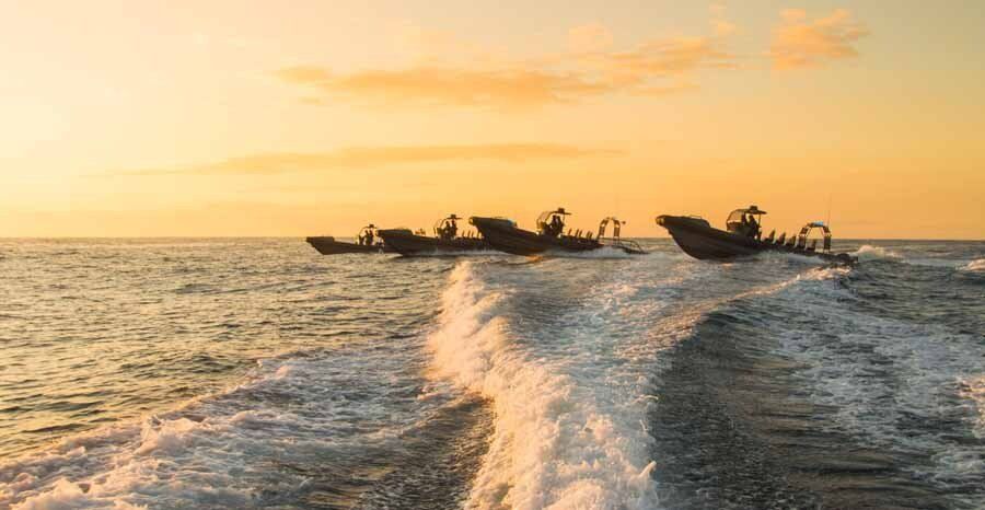 A 3 boats speeding on top of a body of water.