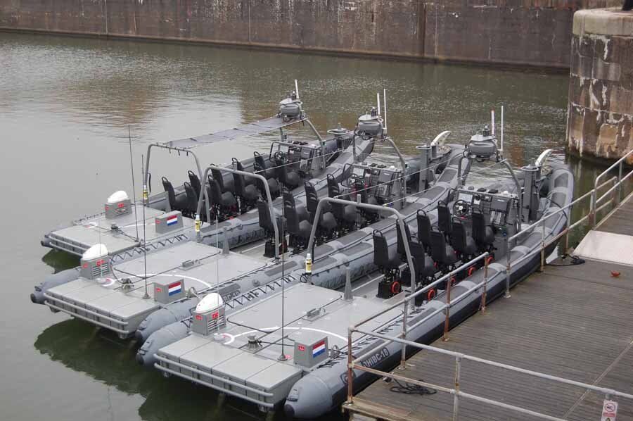 A row of navy boats are docked in a body of water.