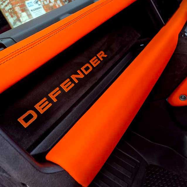 Orange interior trim with “DEFENDER” lettering on a vehicle dashboard panel