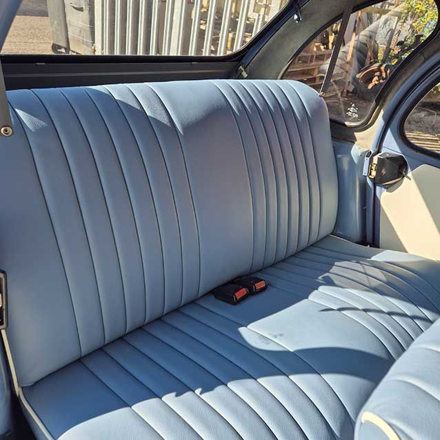 Light blue vinyl car bench seat with a red seat belt buckle in a sunlit interior