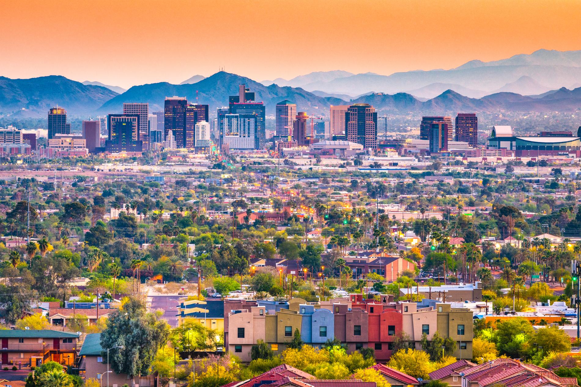Colorful city skyline with mountains in the distance under a warm orange sky