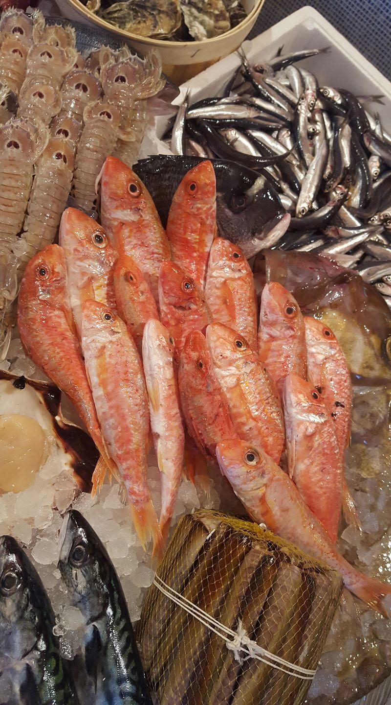 Frutti di mare freschi esposti sul ghiaccio, tra cui pesce rosso, gamberi e piccoli pesci argentati, in un banco del mercato.