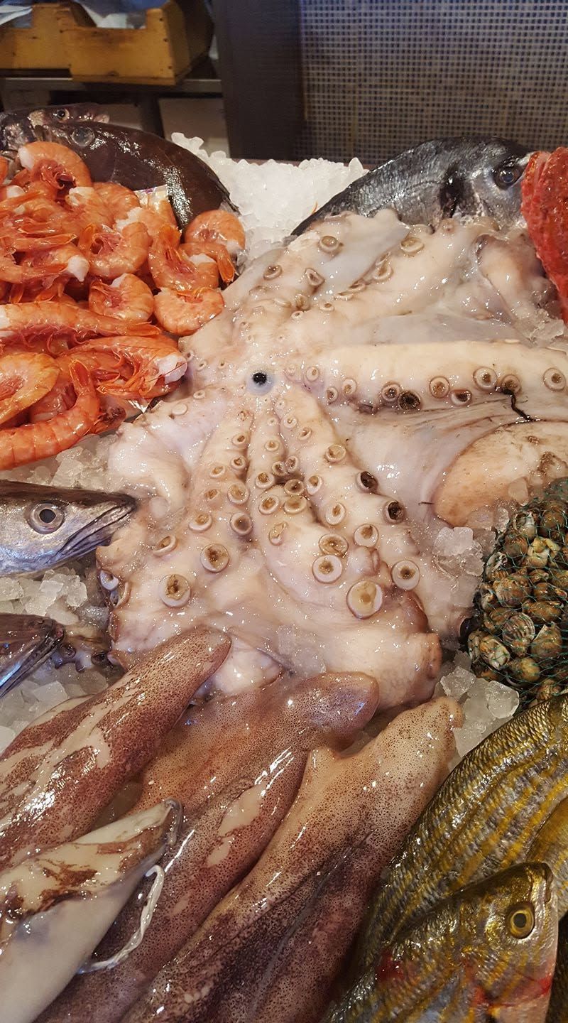 Esposizione di frutti di mare con gamberi, un grosso polpo e altri pesci su ghiaccio in un mercato
