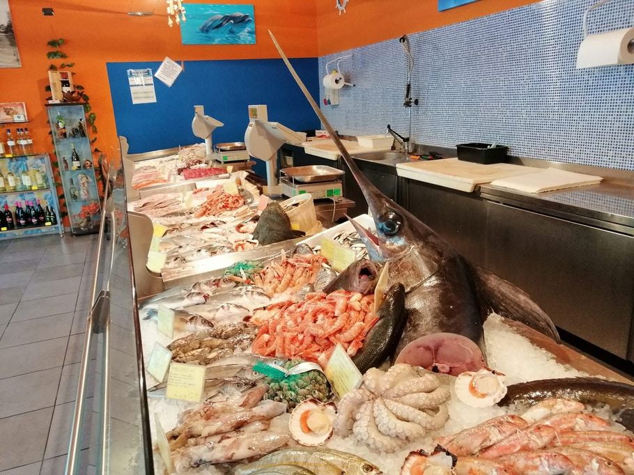 Banco del mercato del pesce con file di pesce fresco, gamberi e molluschi esposti sul ghiaccio sotto luci intense.