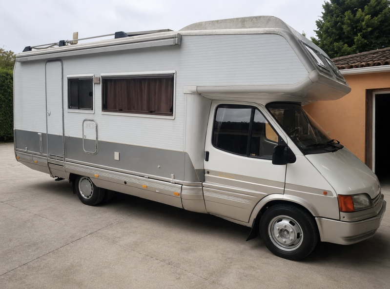 Piccolo camper argentato parcheggiato all'aperto, vista laterale con carrozzeria bianca e grigia.