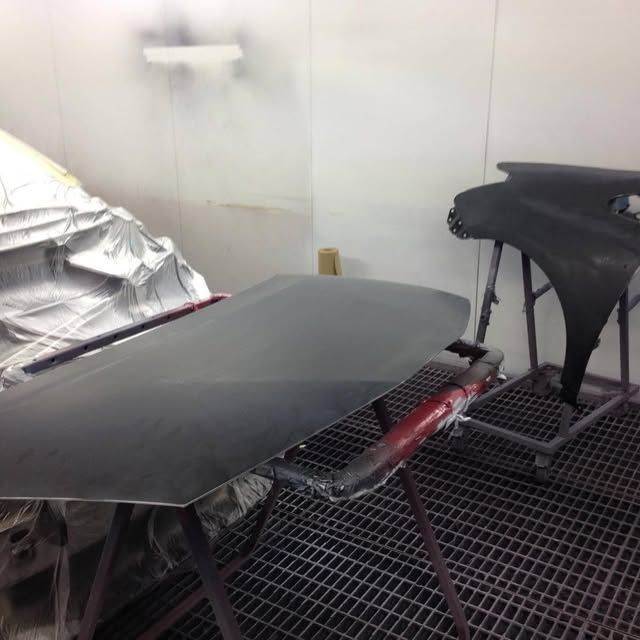 Cabina di verniciatura con due pannelli di carrozzeria neri che asciugano su supporti sopra un pavimento grigliato.