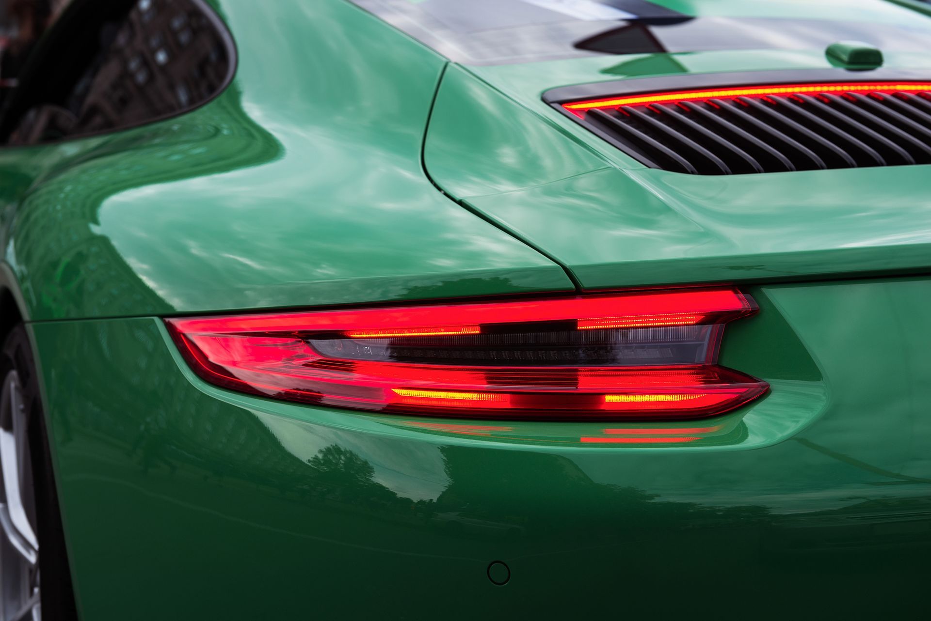 Primo piano del fanale posteriore e del parafango di un'auto sportiva verde con dettagli rossi e neri.