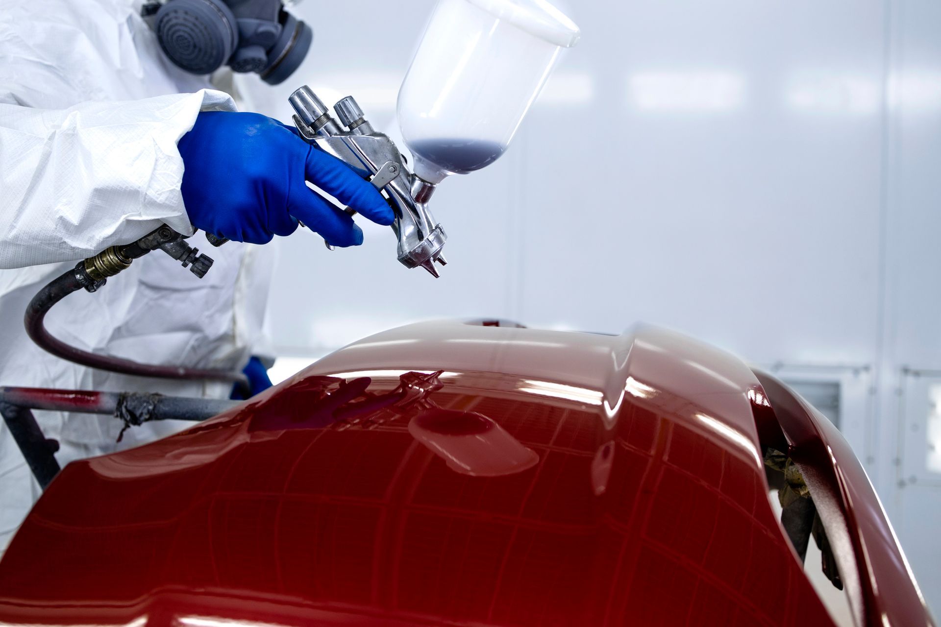 Verniciatore automobilistico che vernicia la carrozzeria di un'auto di rosso lucido in una cabina di verniciatura.
