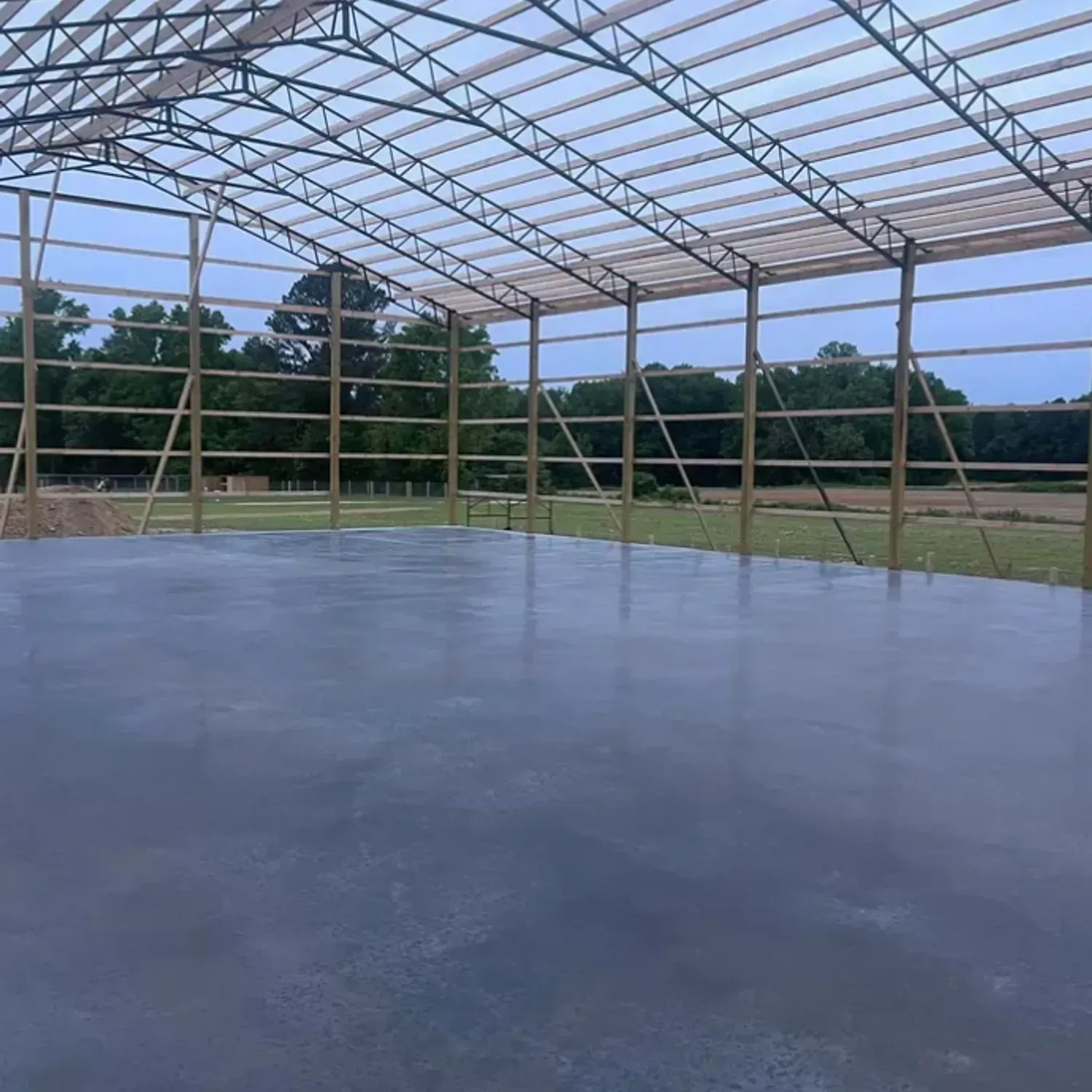 Interior of a metal framed building with a concrete floor, open sides, and a wooded background.