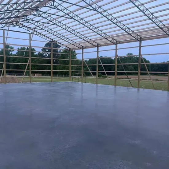 Interior of a metal framed building with a concrete floor, open sides, and a wooded background.