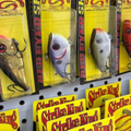 Fishing lures in yellow retail packaging, including red, silver, and gold hard baits on display.