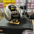 Silver baitcasting fishing reel on a black box with blurred store shelves in the background