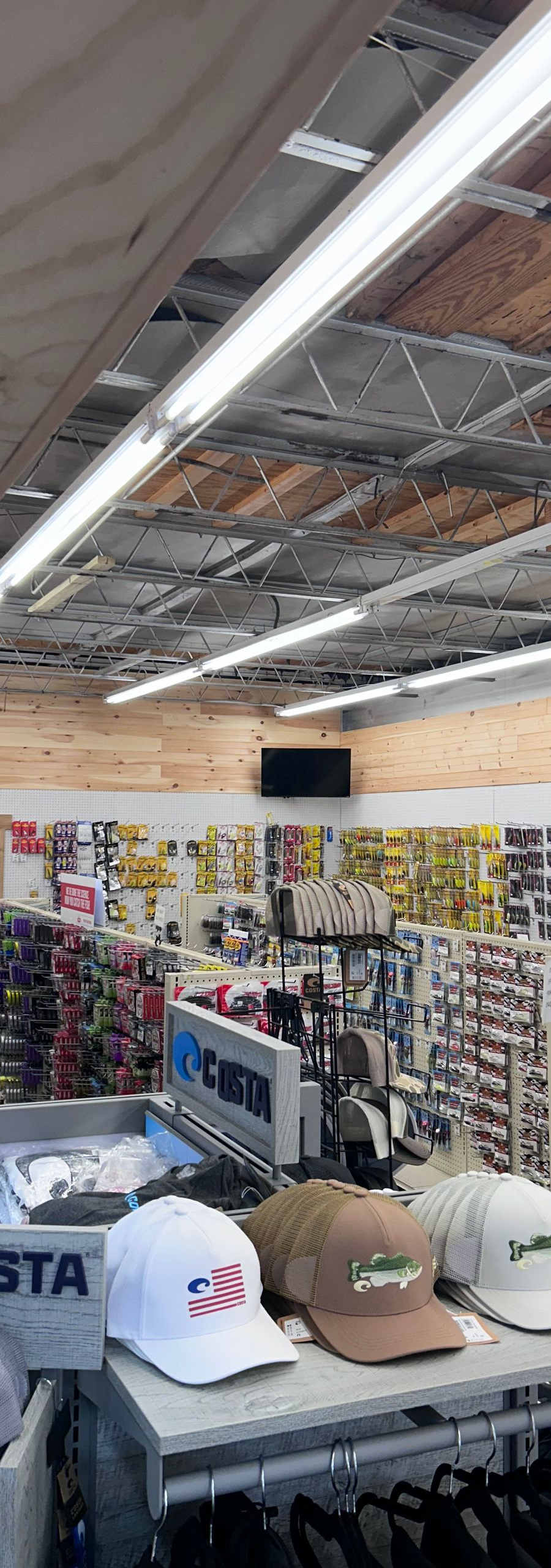 Retail store aisle with shelves of tools and accessories, exposed ceiling, and hats displayed in the foreground