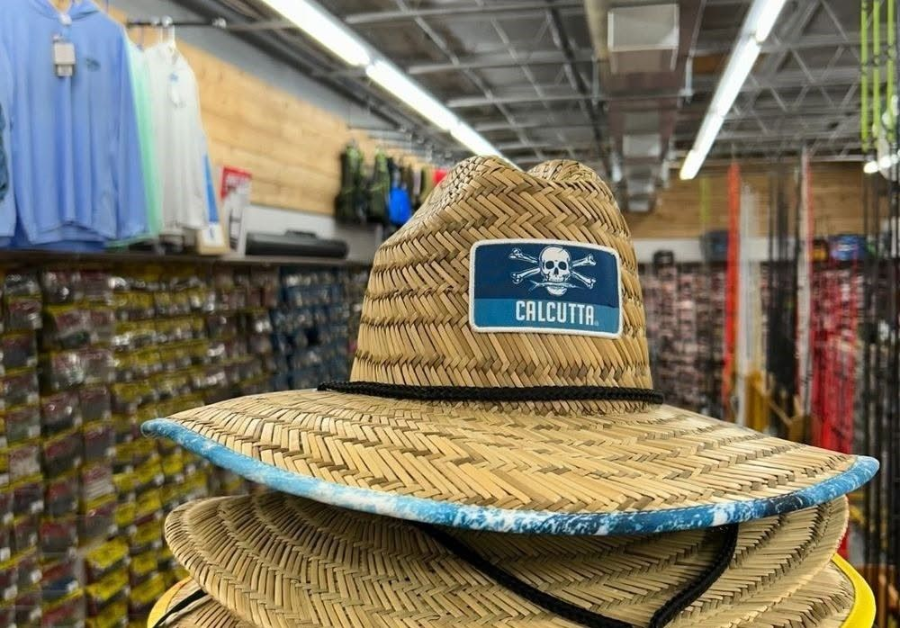 Straw hat with blue “Chilotel” patch displayed on store shelf among other hats and clothing