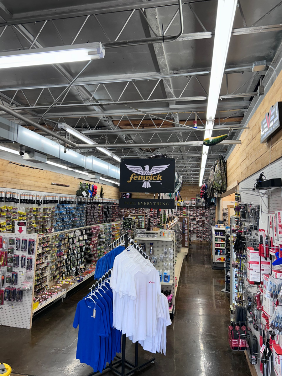 Clothing store aisle with racks of T-shirts and hanging sports apparel under bright warehouse lighting